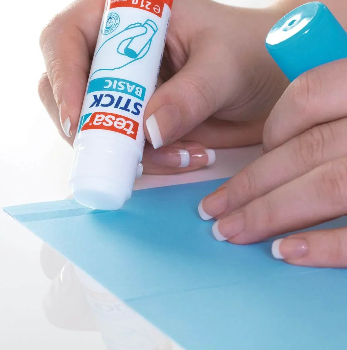 Cola Multiusos Bastão Tesa sendo aplicada em papel azul, mostrando a ponta do bastão de cola.