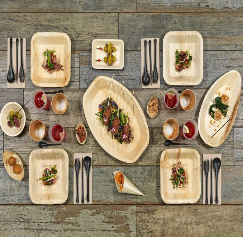 Bandeja Canoa Oval de Folha de Palmeira com pratos e talheres em um serviço de catering elegante.