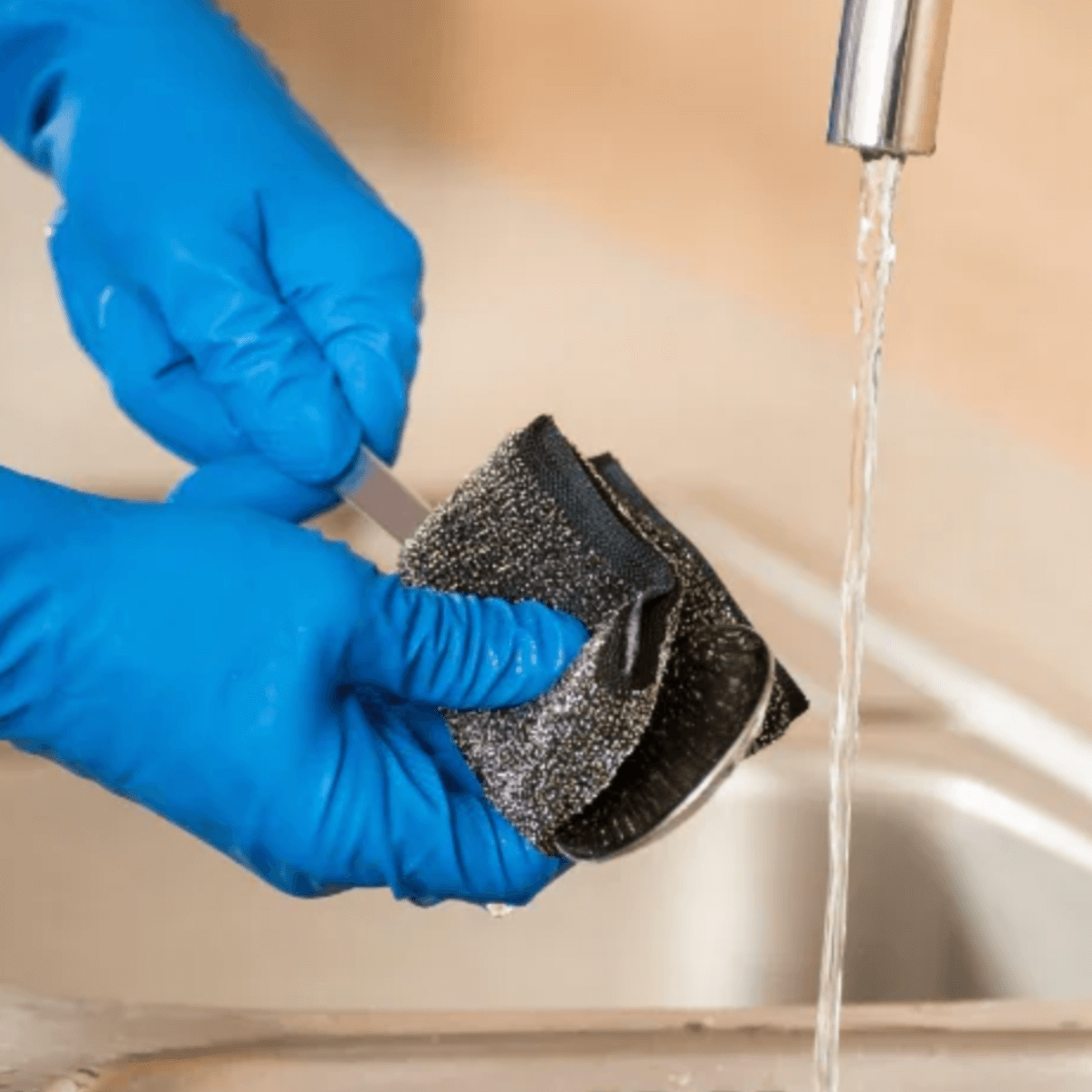 Pessoa a usar o Esfregão Esponja Inox Profissional sob água corrente na pia.